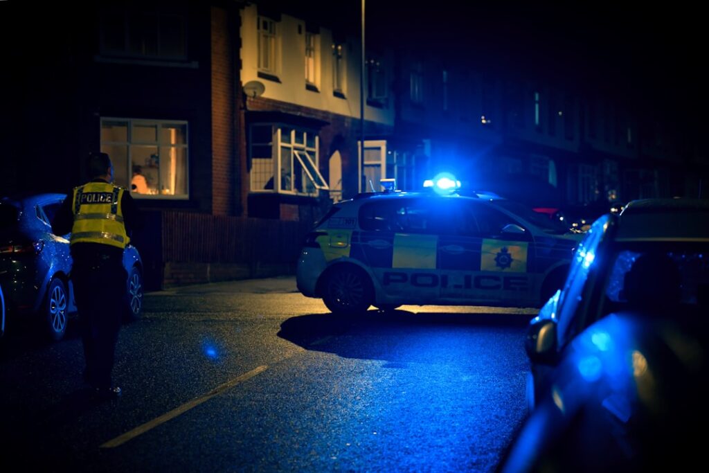 Police officer investigating a crime scene at night with patrol vehicles and emergency lights